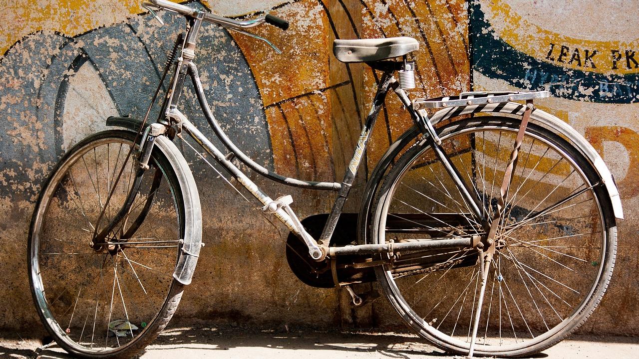 old white bicycle leaning against wall with faded mural