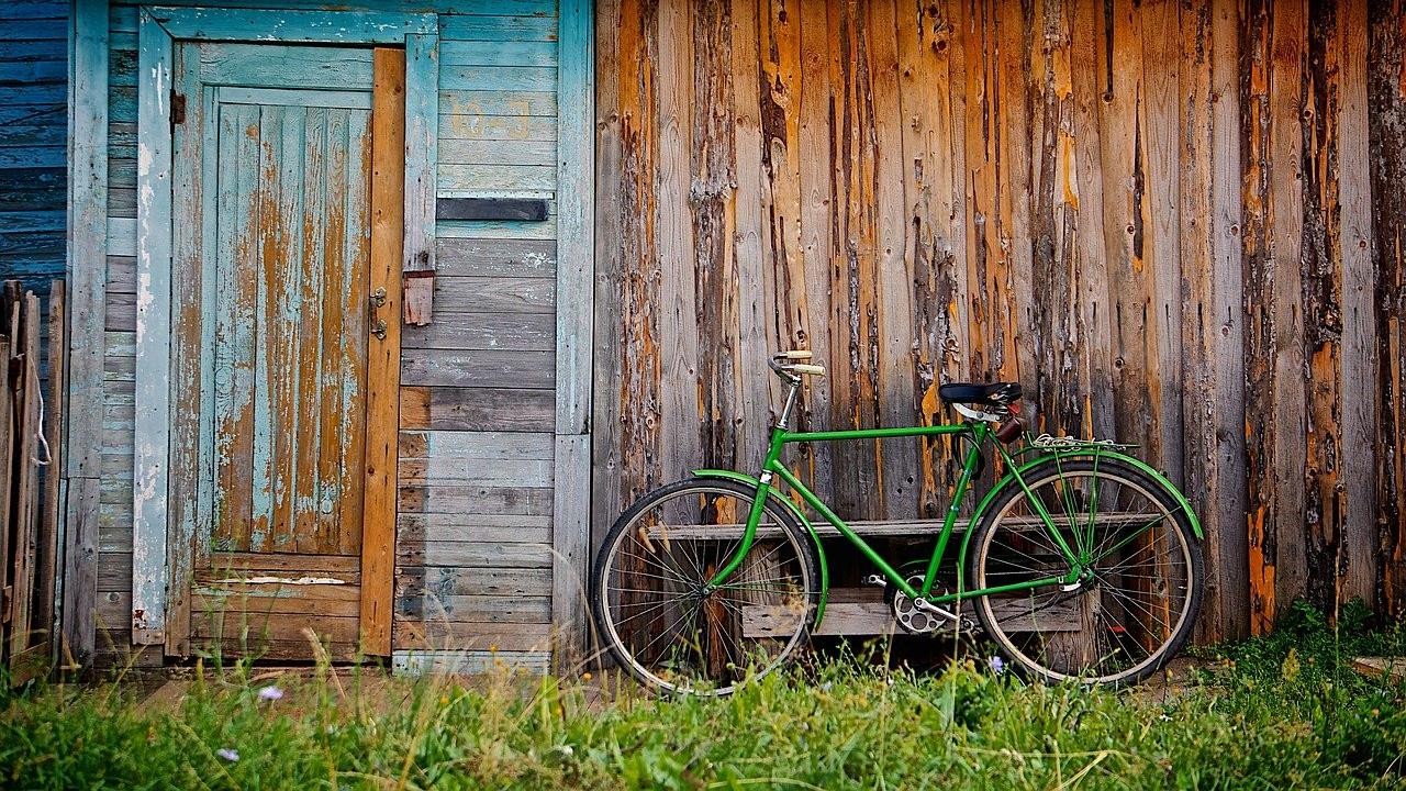 Green bicycle leaning against rustic shed